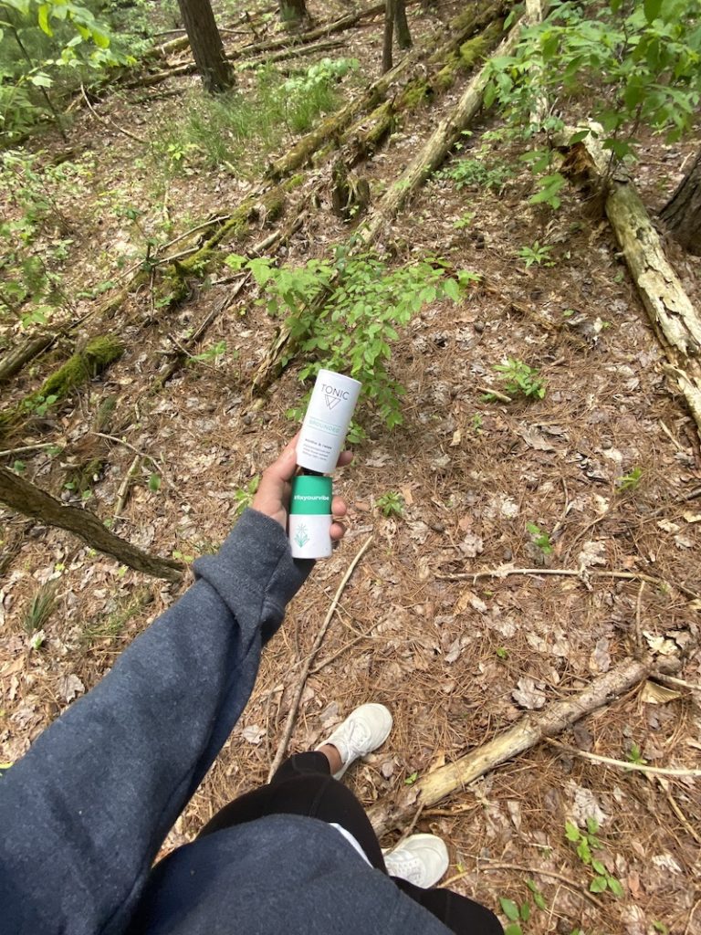 woman holding Grounded-TONIC whole plant hemp extract CBD oil in a wooded forest
