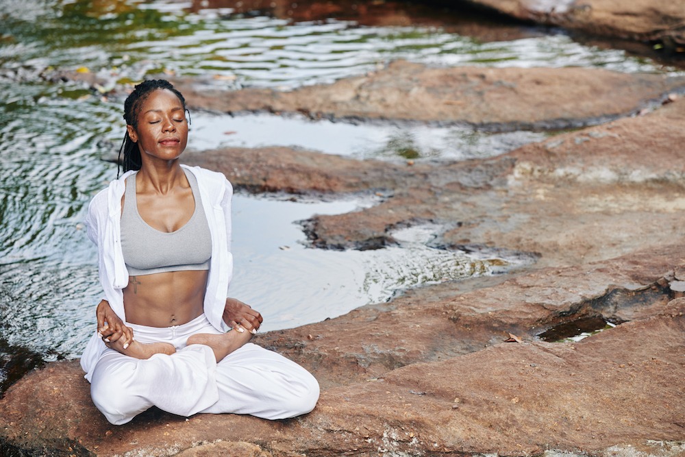 woman sitting on rocks in a stream meditating legs crossed eyes closed